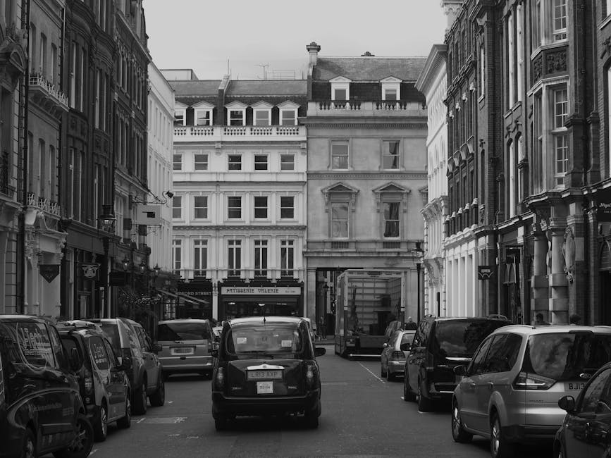 A red double-decker bus numbered 24 is stopped at a busy city intersection outside a row of ornate, classical-style white buildings with multiple large windows and decorative cornices. The bus display